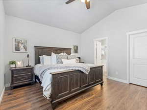 Bedroom with dark hardwood / wood-style flooring, vaulted ceiling, ceiling fan, and ensuite bathroom