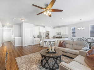 Living room featuring ceiling fan with notable chandelier and dark hardwood / wood-style flooring