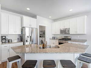 Kitchen with appliances with stainless steel finishes, a breakfast bar, a kitchen island with sink, and white cabinets