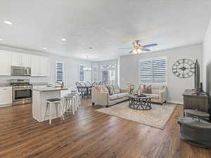 Living room featuring dark wood-type flooring and ceiling fan with notable chandelier