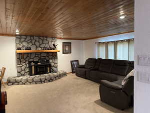 Carpeted living room featuring ornamental molding, a stone fireplace, and wood ceiling