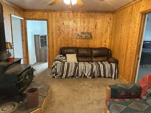 Living room with carpet floors, wooden walls, ceiling fan, and a wood stove