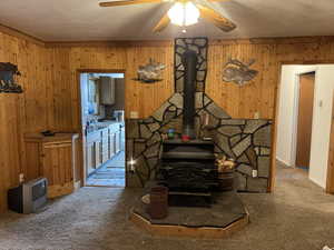 Living room with wooden walls, carpet, ceiling fan, and a wood stove