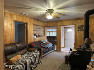 Carpeted living room with ceiling fan, wooden walls, a textured ceiling, and built in features