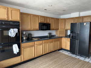 Kitchen featuring tasteful backsplash, light tile patterned flooring, a textured ceiling, and black appliances