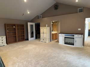 Unfurnished living room with light carpet and high vaulted ceiling