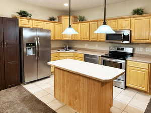 Kitchen featuring light tile patterned floors, sink, hanging light fixtures, stainless steel appliances, and a center island