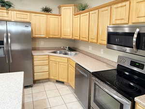Kitchen with appliances with stainless steel finishes, sink, light tile patterned floors, and light brown cabinets