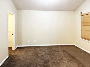 Spare room featuring vaulted ceiling and dark colored carpet