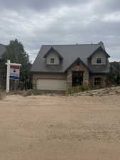 View of front facade featuring stone siding, dirt driveway, a metal roof, and an attached garage
