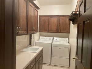 Laundry room with cabinets, sink, light tile patterned floors, and washing machine and clothes dryer