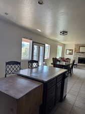 Kitchen featuring a textured ceiling, dark countertops, healthy amount of natural light, a stone fireplace, and light tile patterned floors
