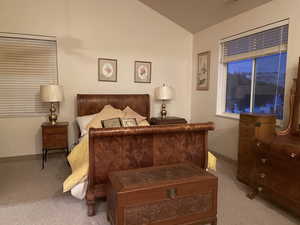 Primary Bedroom with vaulted ceiling and light colored carpet