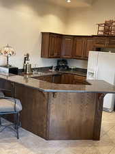 Kitchen featuring a towering ceiling, sink, a kitchen bar, white fridge with ice dispenser, and kitchen peninsula