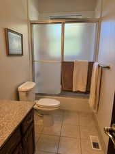 Full bath with bath / shower combo with glass door, vanity, and light tile patterned flooring