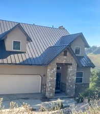 View of front facade with stone siding, a garage, stucco siding, and a metal roof