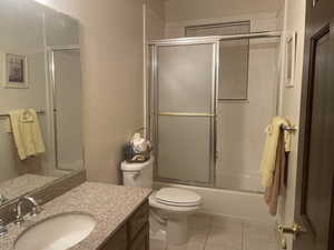 Full bathroom with tile flooring, bath / shower combo with glass door, vanity, and toilet