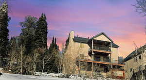 Snow covered back of property with a balcony, a chimney, a metal roof, stucco siding, and a standing seam roof