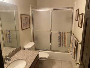 Full bathroom with toilet, vanity, shower / bath combination with glass door, and tile patterned flooring