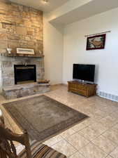 Vaulted living room featuring a stone fireplace and tile patterned flooring