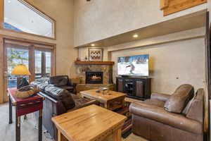 Living room with light carpet, a stone fireplace, french doors, and a towering ceiling