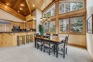 Carpeted dining area featuring a notable chandelier, plenty of natural light, wooden ceiling, and high vaulted ceiling