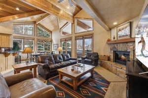 Living room featuring beamed ceiling, plenty of natural light, a stone fireplace, and high vaulted ceiling