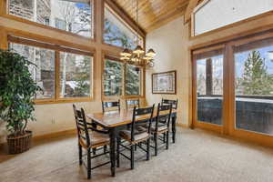 Carpeted dining room featuring a notable chandelier, high vaulted ceiling, and wooden ceiling