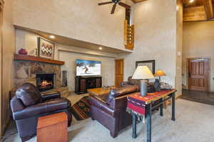 Carpeted living room featuring ceiling fan, a stone fireplace, and a towering ceiling