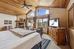 Carpeted bedroom featuring wood ceiling, a stone fireplace, and high vaulted ceiling