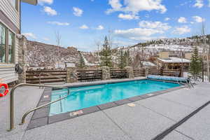 Snow covered pool with a mountain view and a patio area