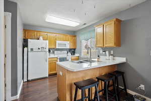 Kitchen featuring sink, white appliances, a kitchen bar, dark hardwood / wood-style flooring, and kitchen peninsula