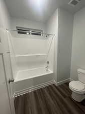 Bathroom with tub / shower combination, hardwood / wood-style floors, and toilet