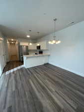 Kitchen featuring white cabinets, stainless steel refrigerator, hanging light fixtures, and dark hardwood / wood-style flooring