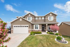 View of front of house with a front yard, covered porch, stone siding, concrete driveway, and stucco siding
