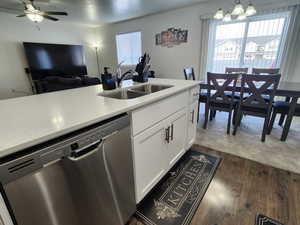 Kitchen with sink, dark wood-type flooring, white cabinetry, hanging light fixtures, and stainless steel dishwasher