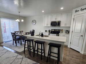 Kitchen with appliances with stainless steel finishes, decorative light fixtures, an island with sink, sink, and white cabinets