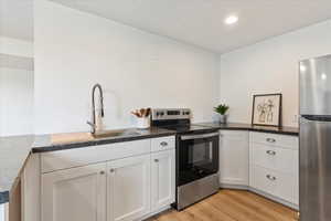 Kitchen featuring stainless steel appliances, sink, white cabinets, and light wood-type flooring