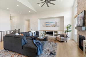 Living room featuring ceiling fan, a stone fireplace, high vaulted ceiling, and light hardwood / wood-style floors