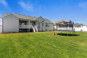 Rear view of property with a trampoline and a lawn