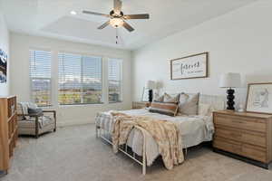 Carpeted bedroom with a tray ceiling and ceiling fan