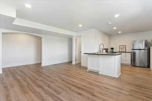 Kitchen featuring white cabinets, sink, stainless steel fridge, and light hardwood / wood-style flooring