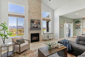 Living room with a mountain view, high vaulted ceiling, a stone fireplace, and light wood-type flooring