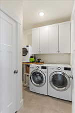 Washroom with cabinets, light tile patterned flooring, and washing machine and clothes dryer