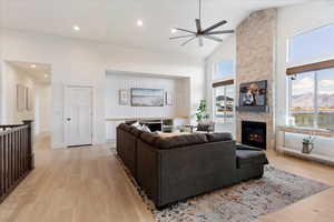 Living room featuring high vaulted ceiling, a healthy amount of sunlight, a stone fireplace, and light hardwood / wood-style floors