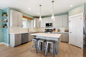 Kitchen featuring sink, hanging light fixtures, stainless steel appliances, a center island, and light wood-type flooring