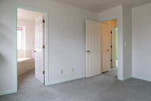 Unfurnished bedroom with ensuite bathroom and light carpet