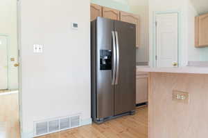 Kitchen with light brown cabinetry, stainless steel fridge, and light hardwood / wood-style floors