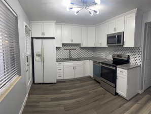 Kitchen with dark hardwood / wood-style flooring, sink, white cabinets, and appliances with stainless steel finishes