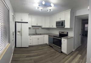 Kitchen with appliances with stainless steel finishes, dark hardwood / wood-style flooring, sink, and white cabinets